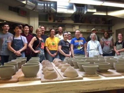 Students stand behind ceramic bowls laid out on a table.