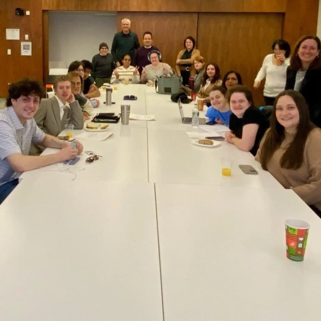 Individuals sit and stand around a table.