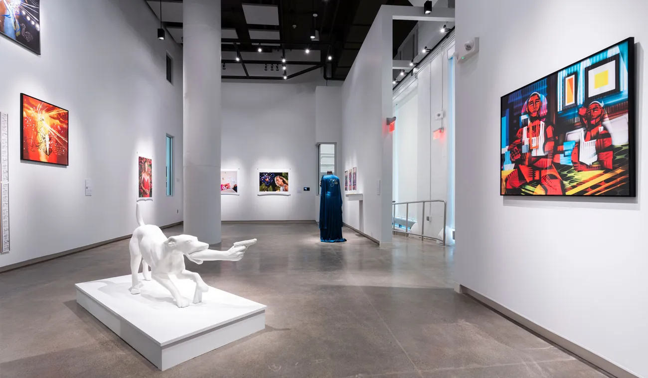 An art gallery with photographs and paintings on the walls and a sculpture in the middle of the floor.