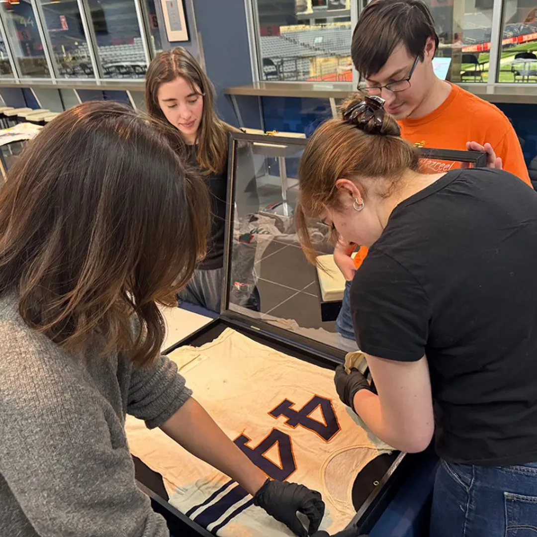 Four students work around a table, arranging an old football jersey with the number 44 on it on a mat prior to being framed.