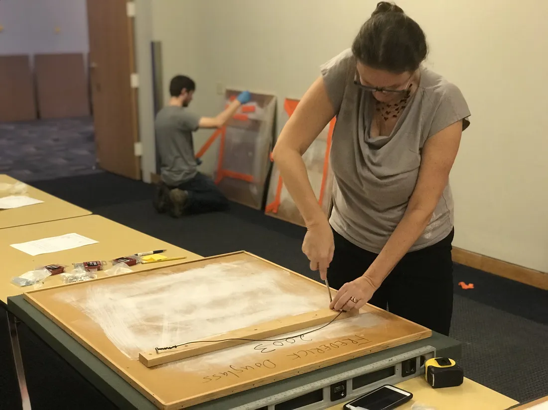 A person prepares a painting for installation on a wall.