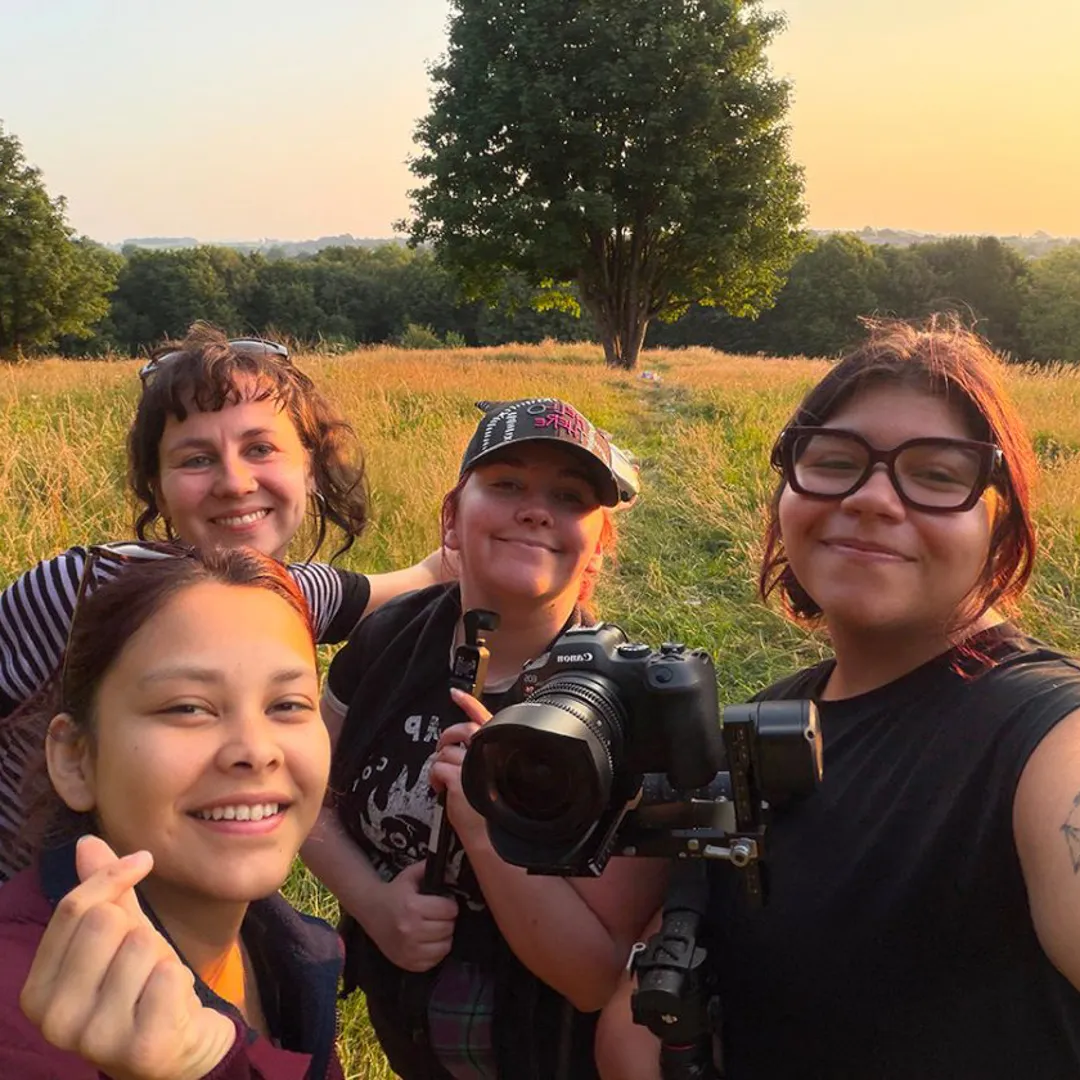 Four people stand in a field. One individual holds a camera.