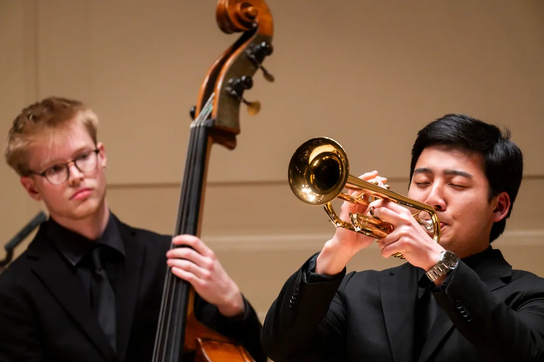 A person plays a trumpet while another person plays double bass.