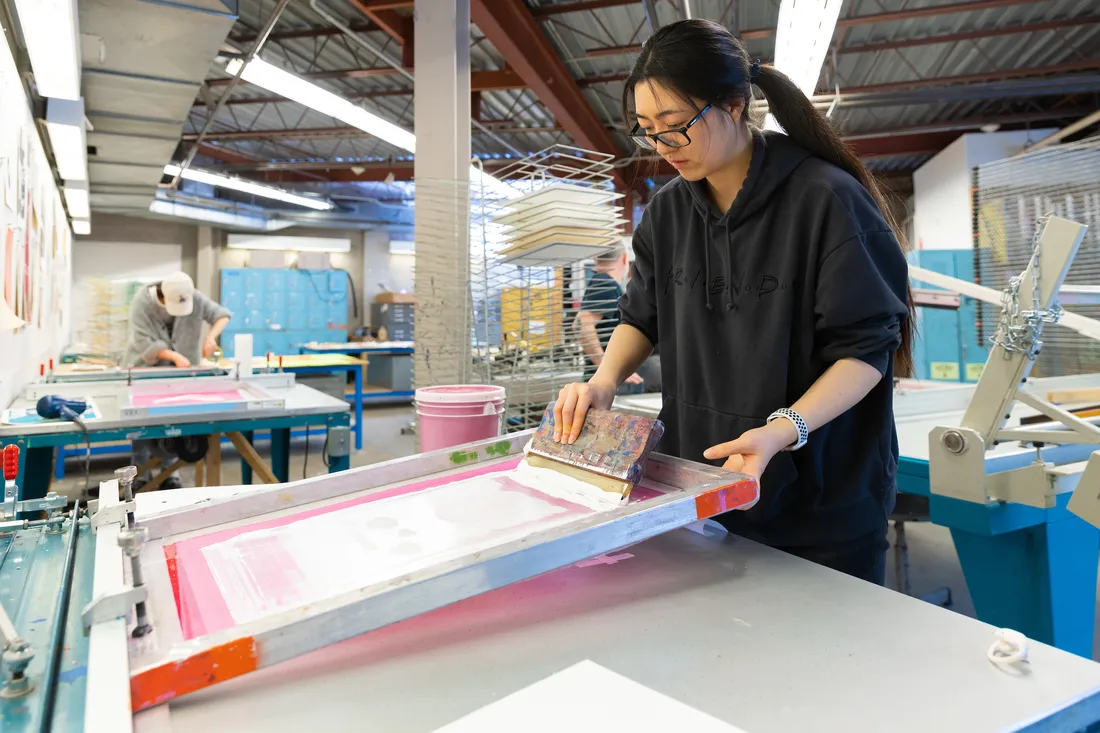 A student uses a screen in a printmaking studio.