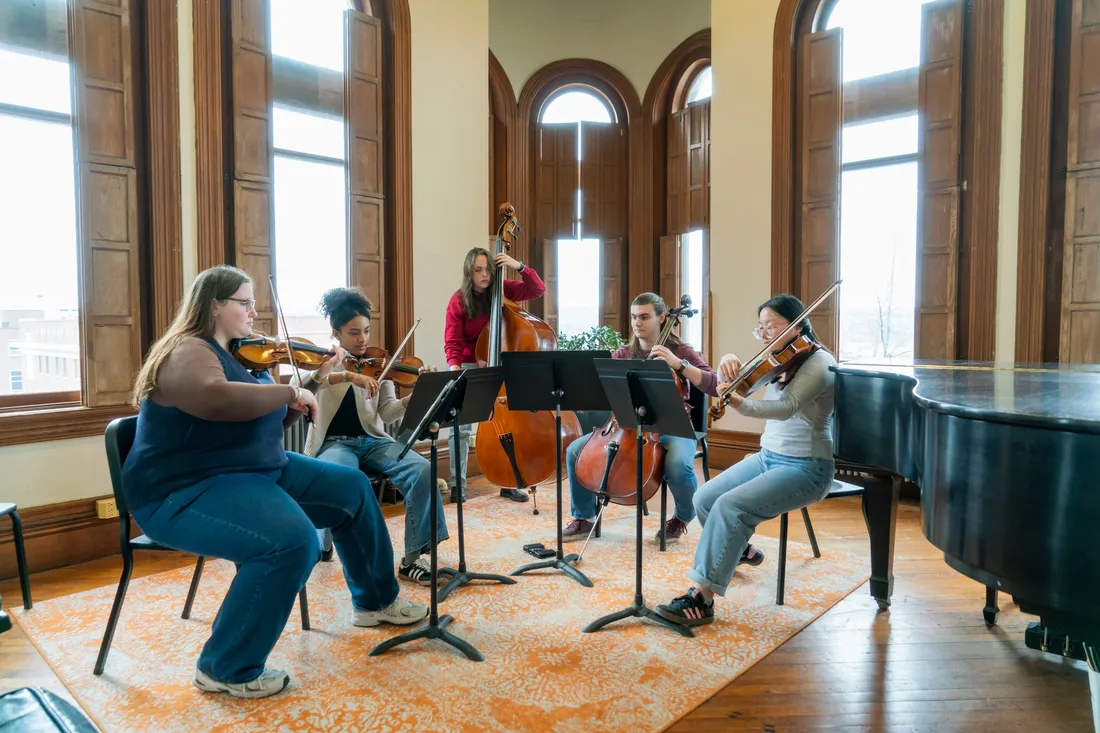 A string quintet practices in a large room with Victorian windows.