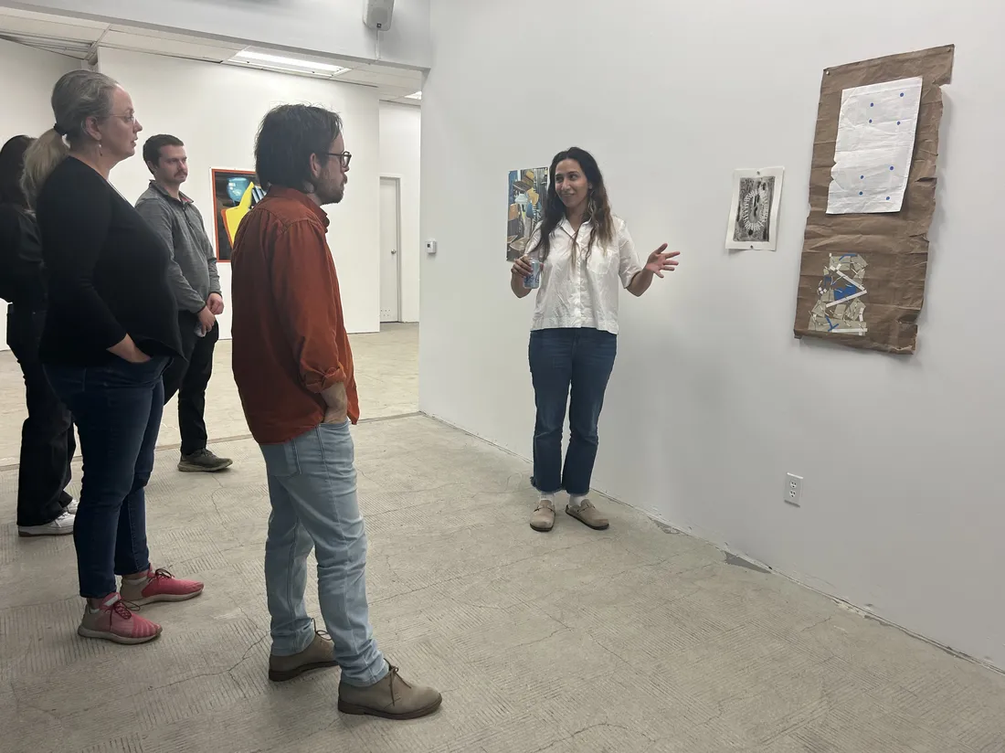 A student gestures to a piece of artwork on a gallery wall and talks to three people who are looking at the artwork.