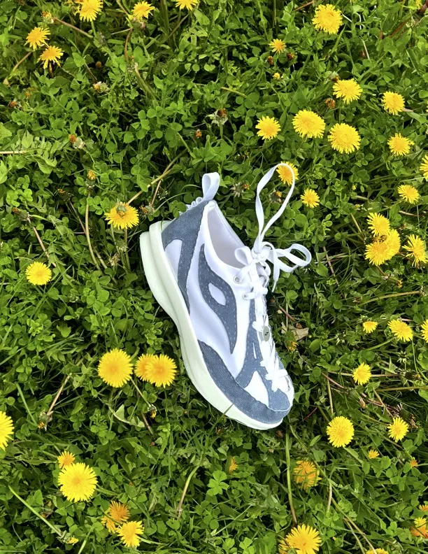 A shoe on grass, surrounded by flowers.