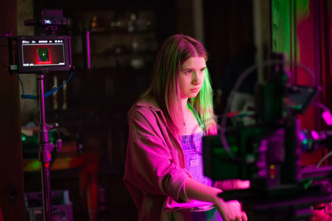A student stands near a camera on the set of a film shoot.