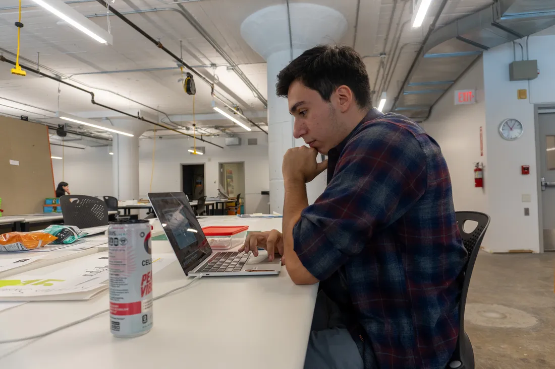 A student sits at a table looking at a laptop.