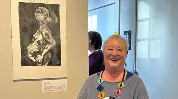 Adair Hietmann stands next to a lithograph of a pregnant woman hanging on a wall in a gallery.