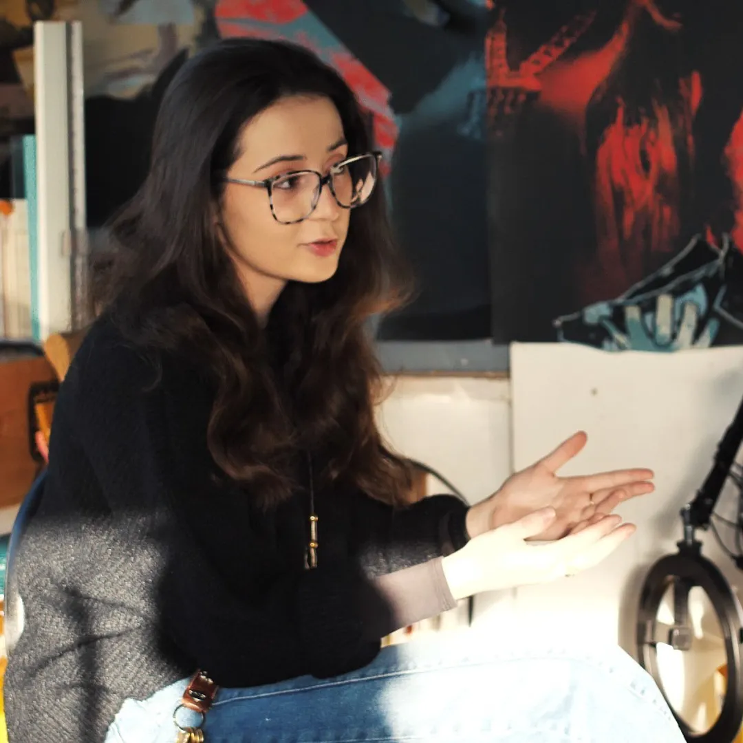 Sophia Hashemi sits at a chair, speaking and moving her hands.