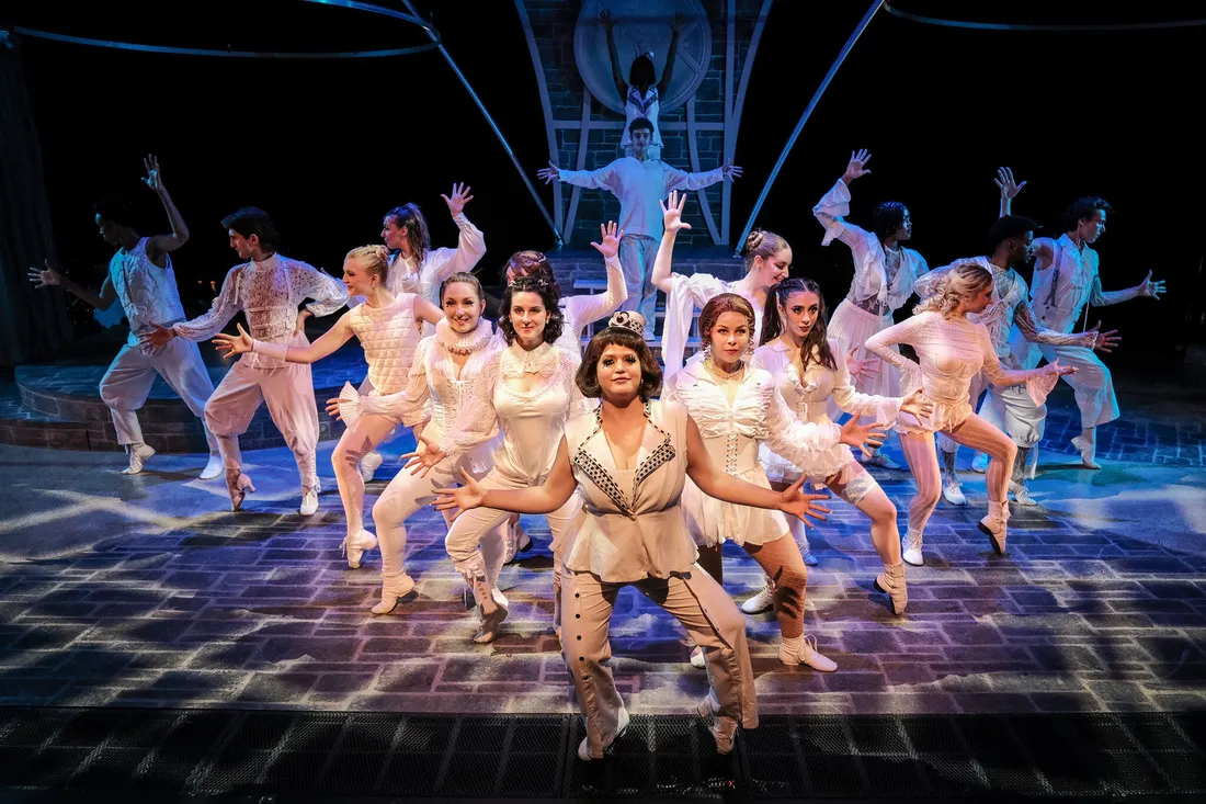 A large group of students in costume perform a dance number on a stage.