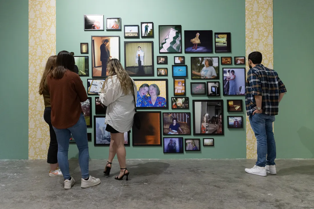 A group of people stand and look at a collection of photographs displayed on a gallery wall.