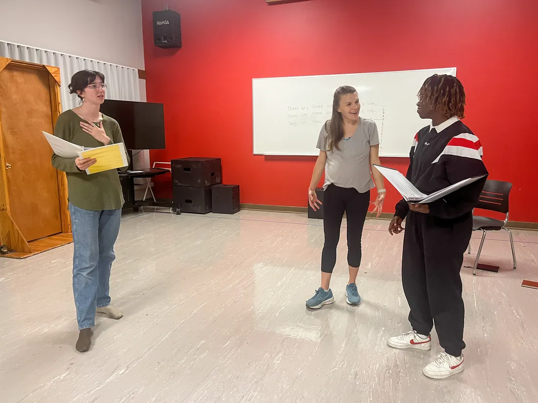 Two students hold scripts and a faculty member directs them in an acting studio.