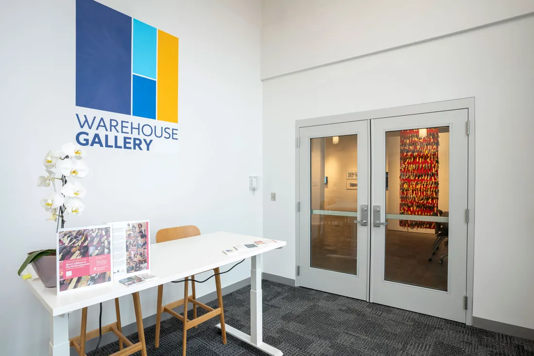 The entrance to a gallery with a table and chairs and sign that says Warehouse Gallery