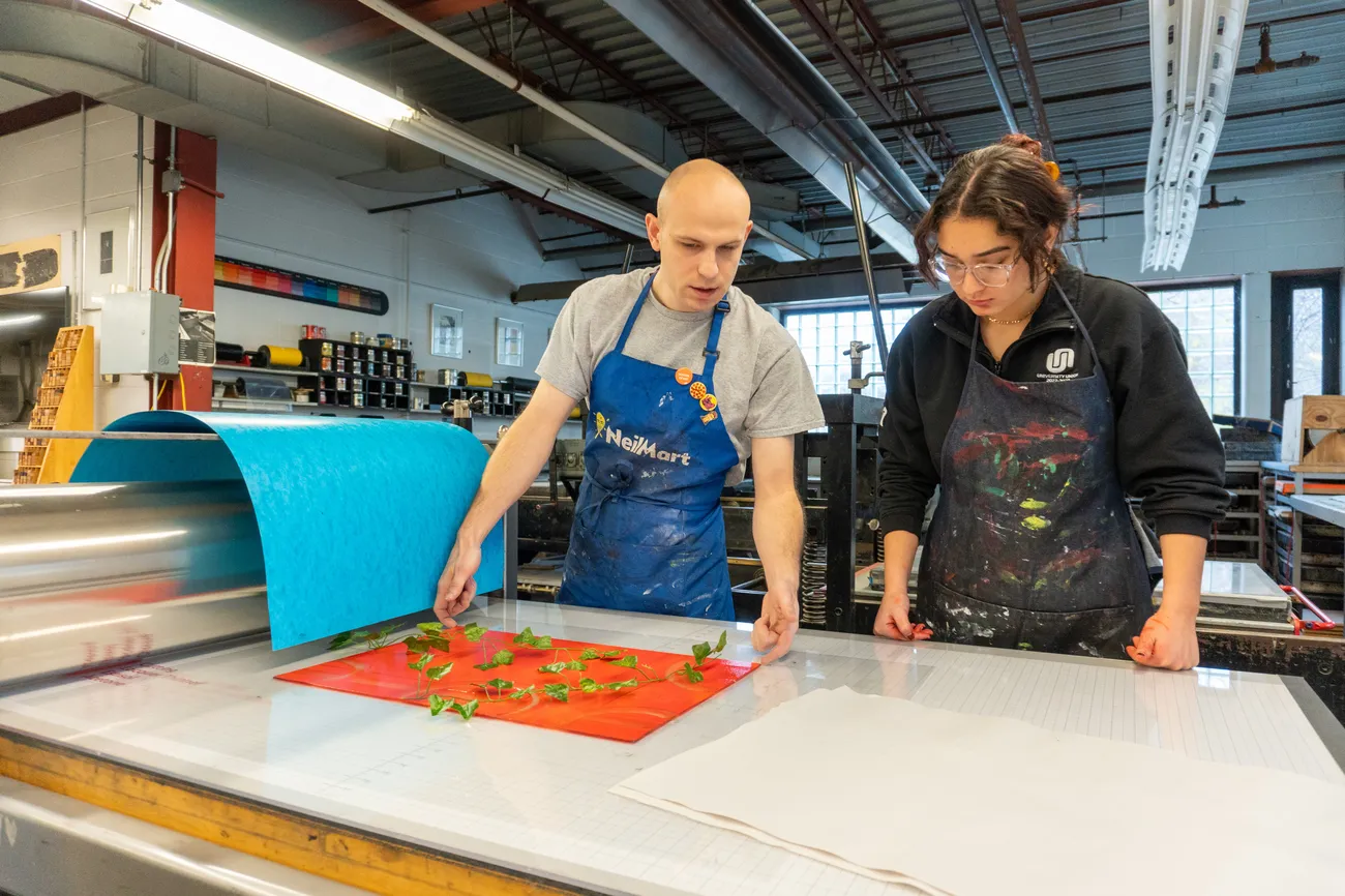 A teacher and student work on a print in a printmaking studio.