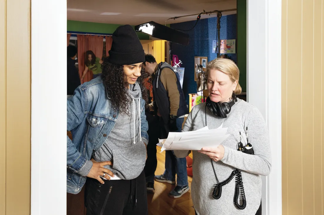 Two people stand in a doorway on a film set looking at a set of papers.
