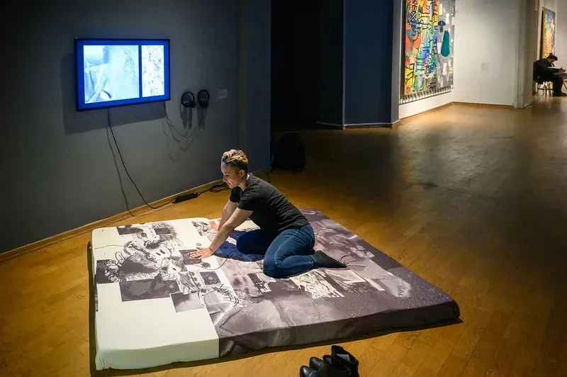 A person sits on a large square of memory foam that has images printed on it.