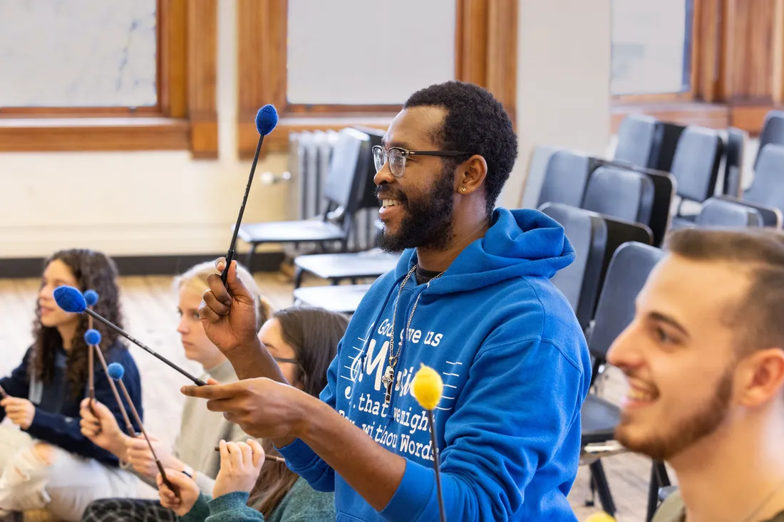 A student smiles in a classroom and holds percussion mallets.
