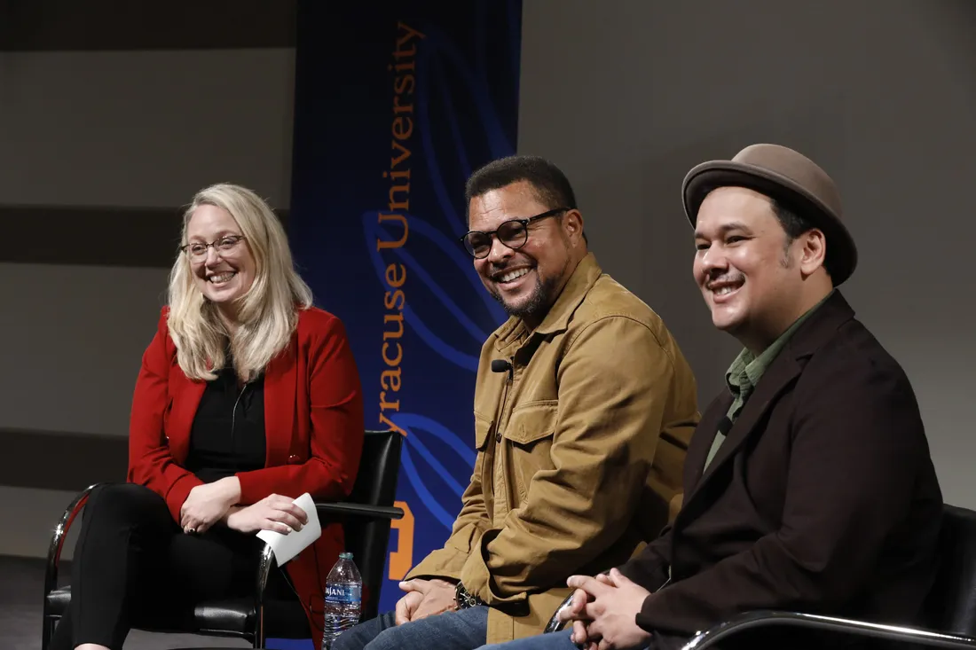 Three people sit on a stage smiling.
