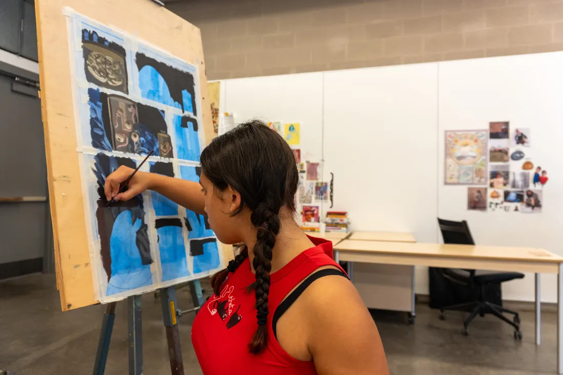 A student paints on a canvas on an easel.