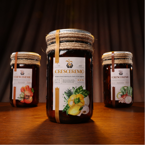 Three rustic jars of “CresCremo” preserved foods are displayed on a wooden table under warm lighting, featuring decorative rope-wrapped lids and illustrated labels with fresh vegetables and fruits. The center jar is highlighted in the foreground, creating an artisanal gourmet presentation.