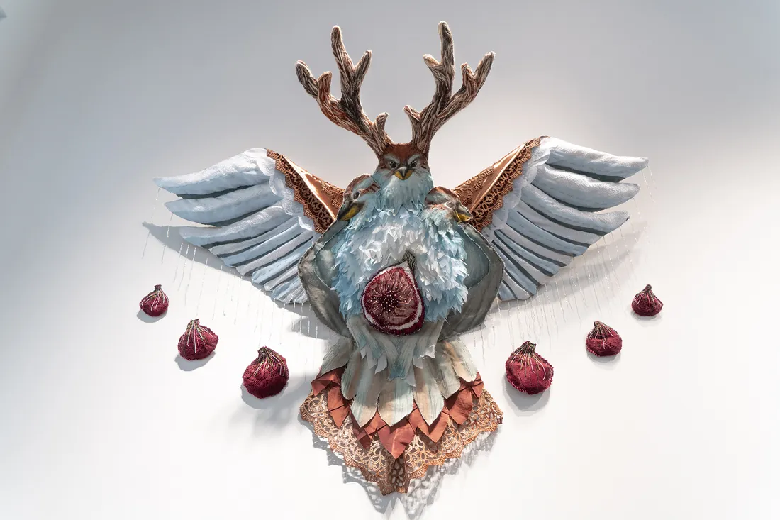 A ceramic work mounted on a gallery wall of a bird-like creature with antlers.