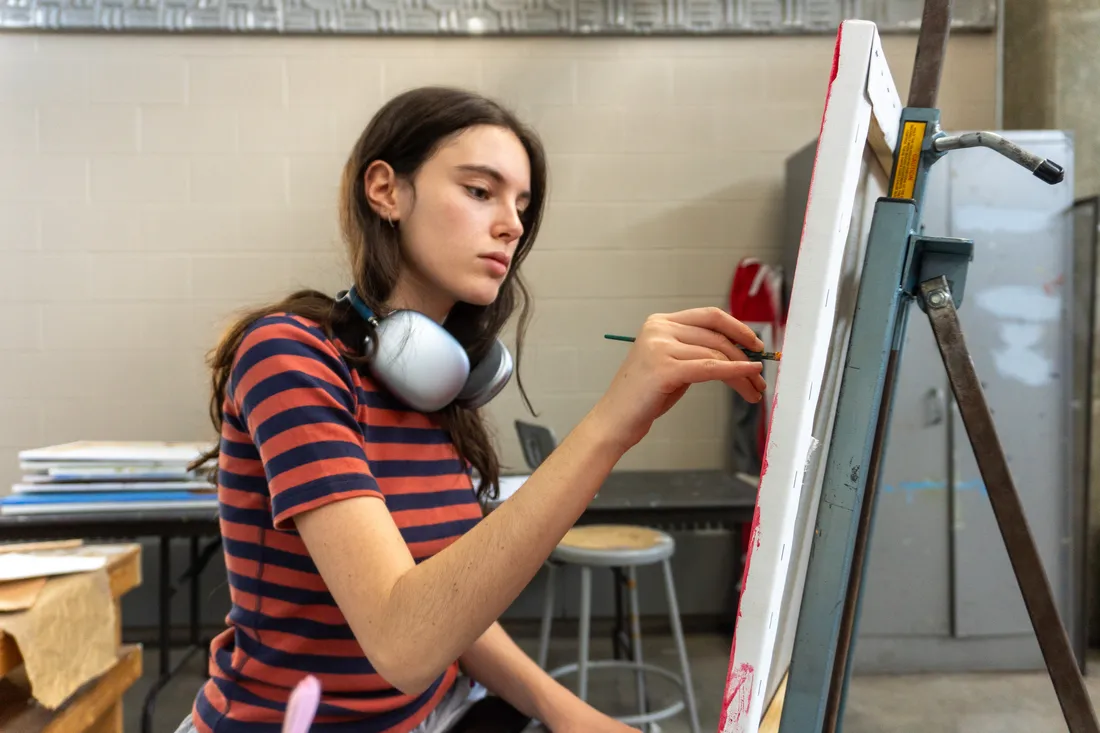 A student paints on a canvas on an easel.