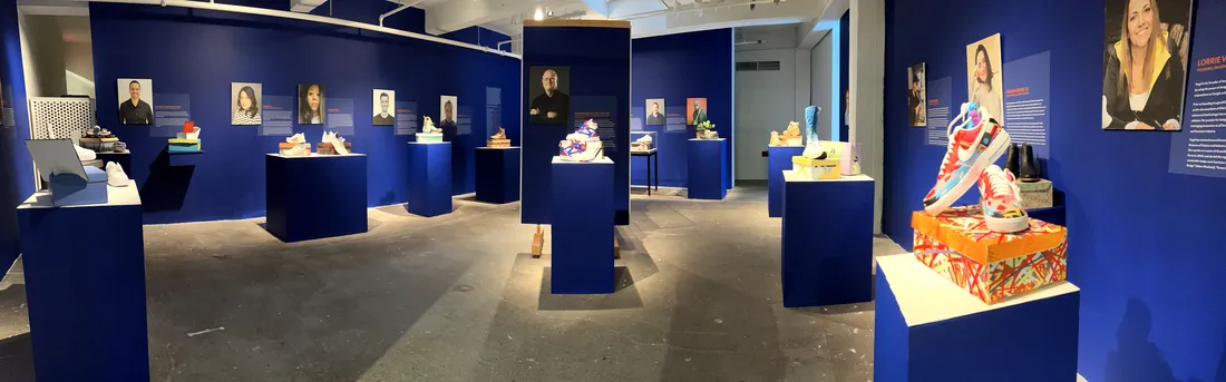 A gallery displaying footwear on pedestals and in glass cases. On the walls are pictures of designers.