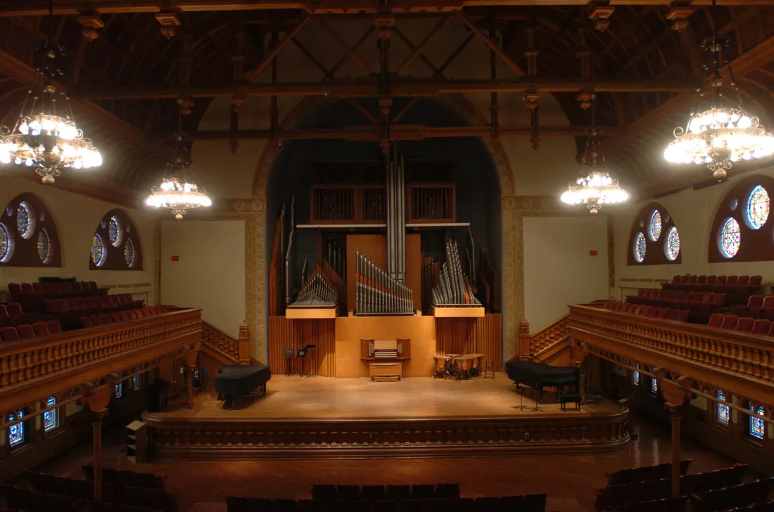 A view of an empty, historic auditorium from the back. It is dimly lit and features a large organ on stage.