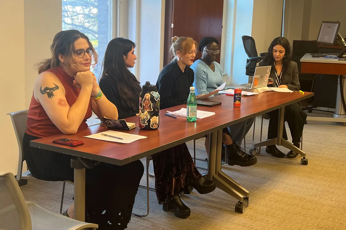 Five students sit in a row at a table in a classroom.
