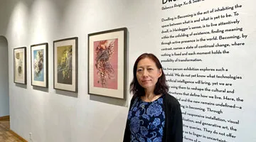 Rebecca Ruige Xu stands in front of a gallery wall with artworks and text on the wall.