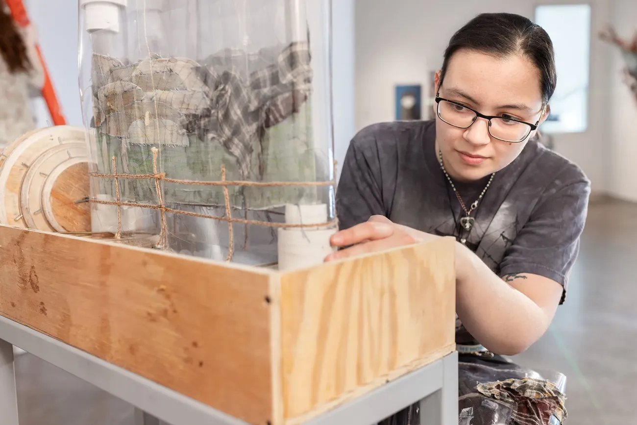 A student works on a sculpture made of mixed materials including wood.