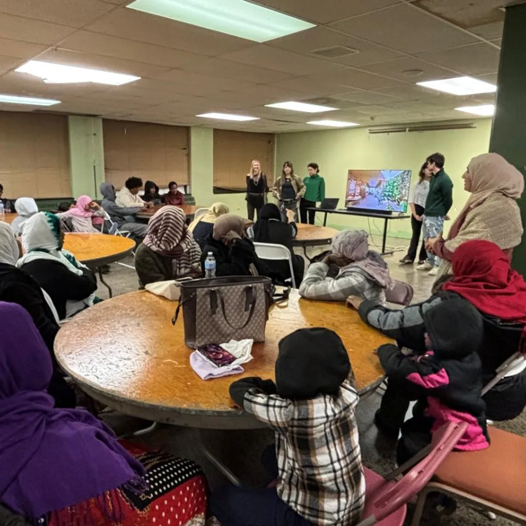 People sit at tables, listening to a speaker.