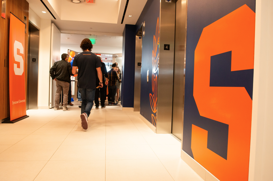 A student walks down a hallway with elevator doors on one side.