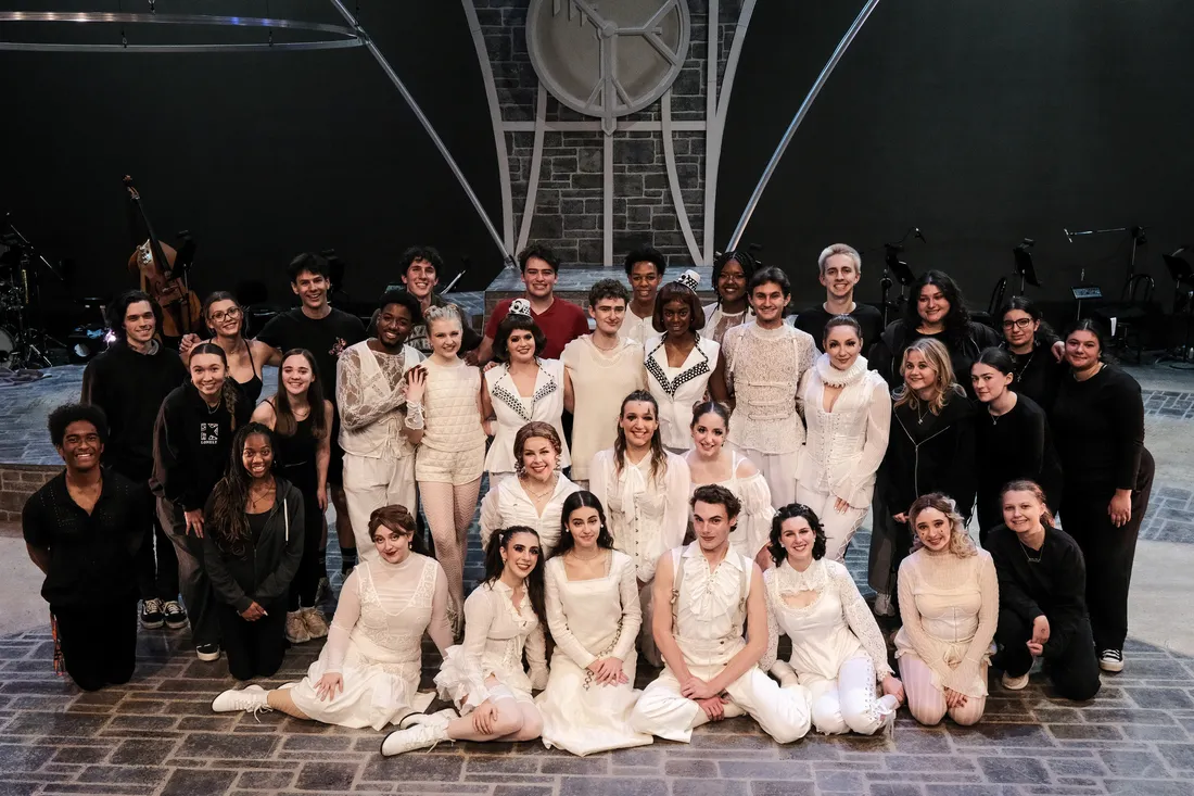 A group of cast and crew members pose and smile on a stage.