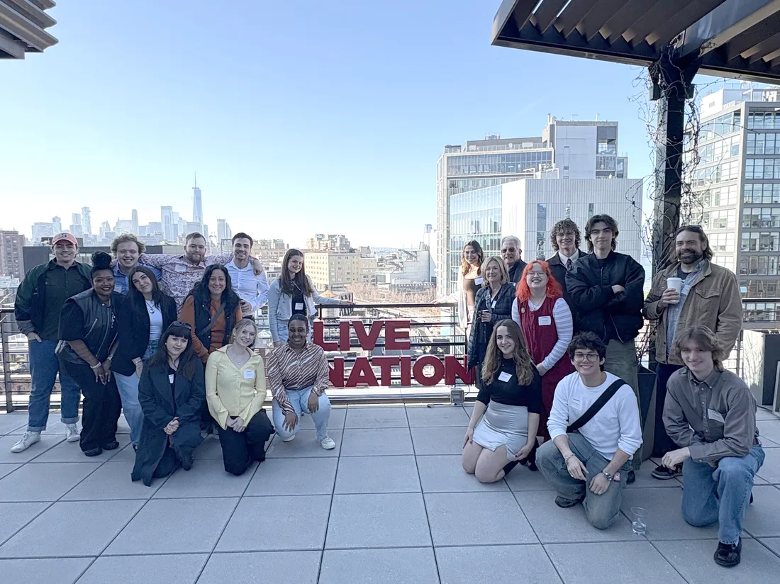 A group of students pose and smile on an outdoor terrace overlooking New York City. A sign reading Live Nation is affixed to the terrace's railing.
