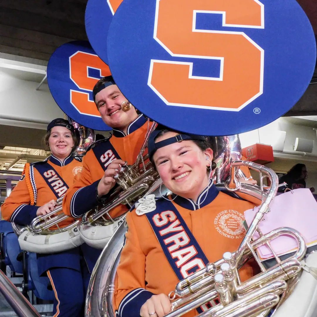 Three individuals hold instruments and smile.