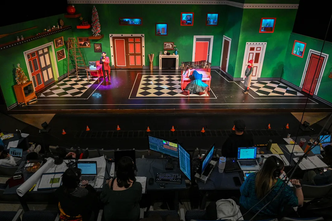 A wide view of a set with crew members sitting in the dark at the bottom of the photo.