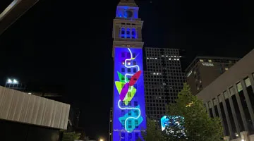A clocktower at night with a colorful animation projection on one side.