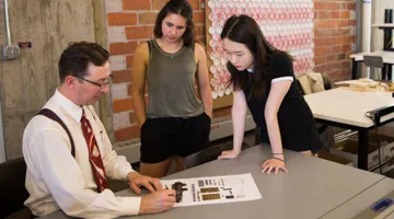 A professors points to a piece of paper in front of two students.