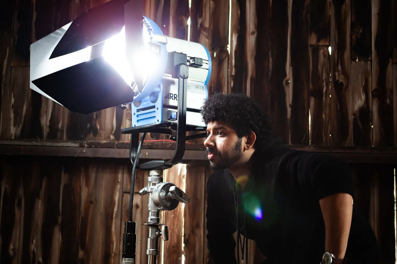 A student stands next to a large light on a film set.