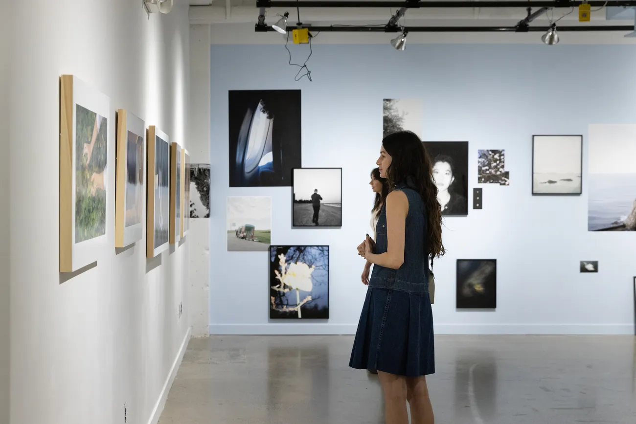 Two people stand in a gallery looking at a wall of photographs.