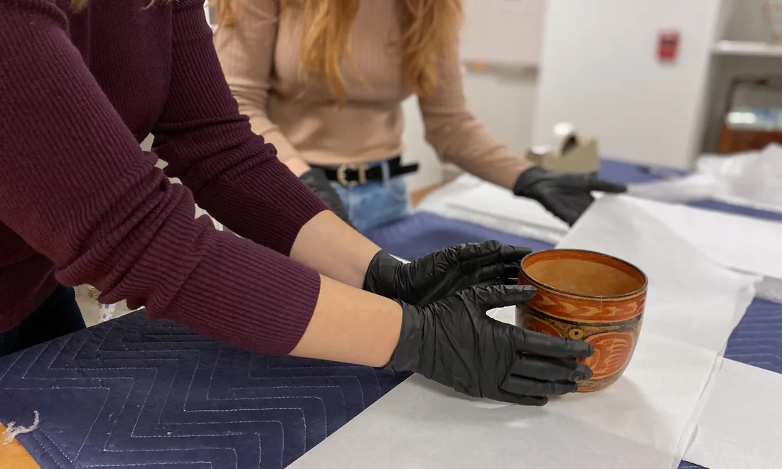 Two hands wearing black gloves handle a ceramic bowl.