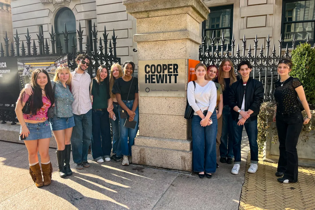 Students stand beside a pillar with lettering that reads “Cooper Hewitt.”