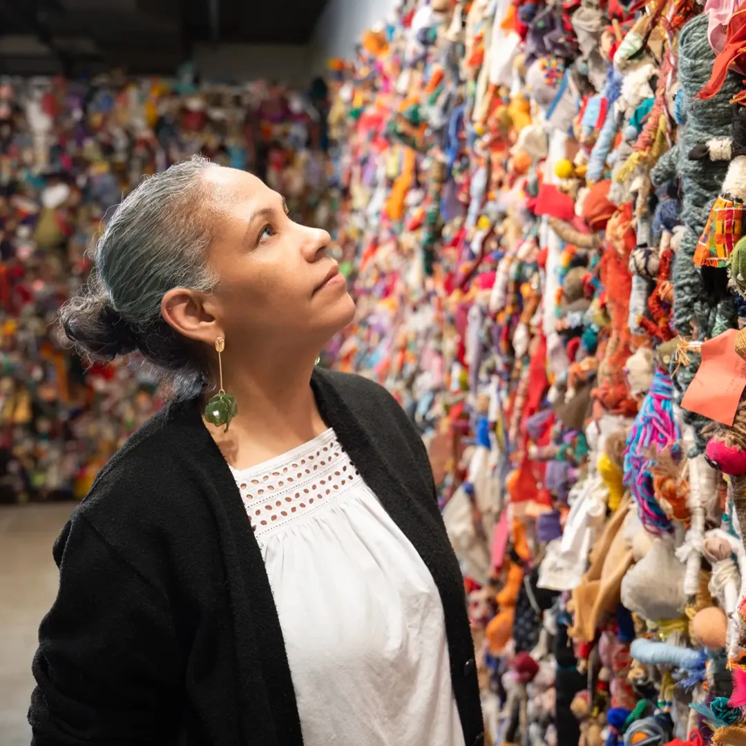 Rochele Royster looks up at a wall of colorful fabric dolls.