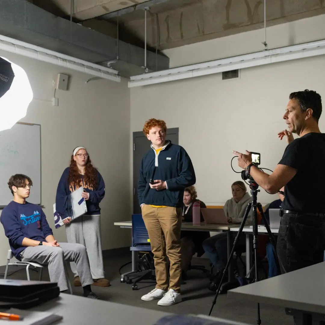 Michael Hicks speaks with students in a classroom with camera equipment set up.
