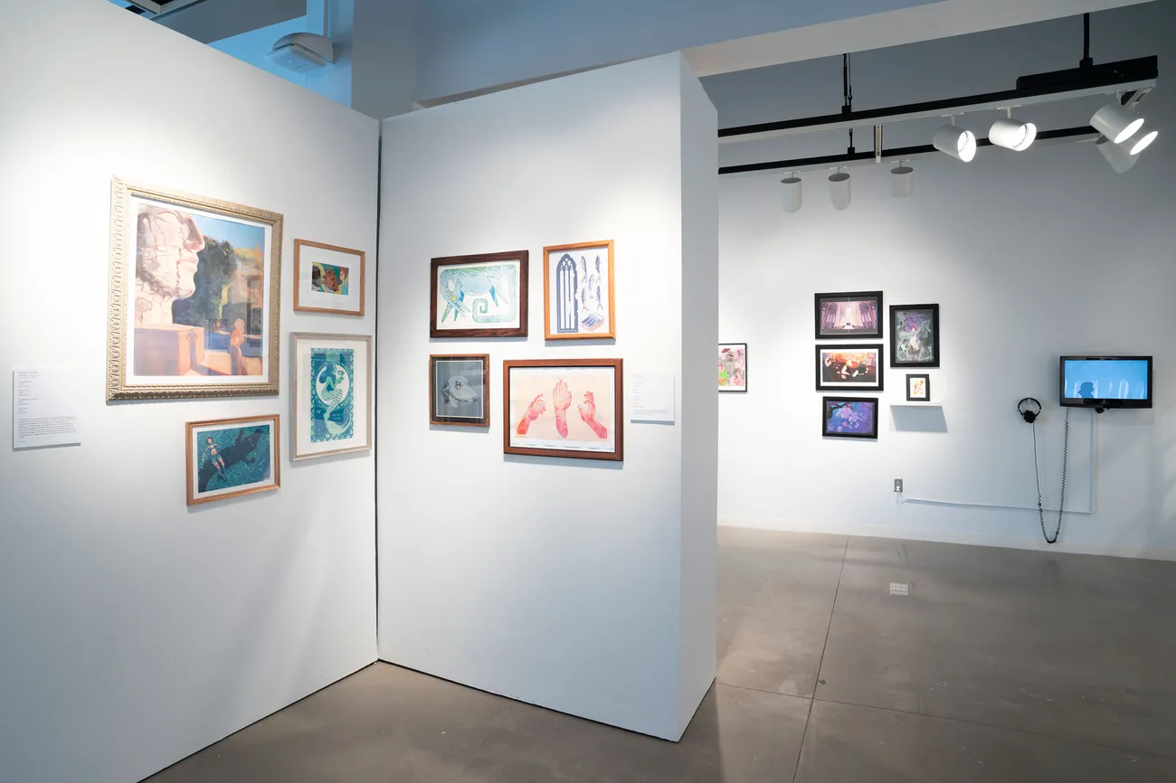 A gallery space with framed artwork hanging on walls and a digital screen.