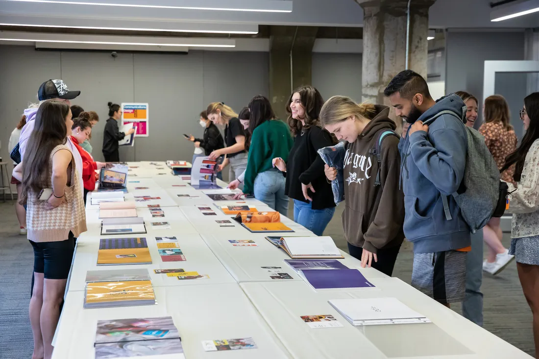 Students stand at a table looking at portfolios of design work.
