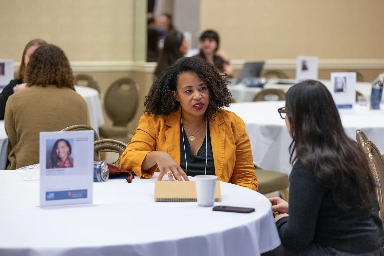 An alumna and a student sit at a table and talk.